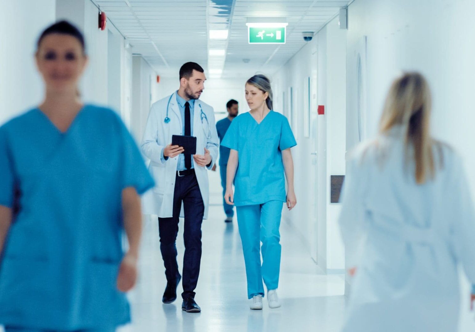Surgeon,And,Female,Doctor,Walk,Through,Hospital,Hallway,,They,Consult